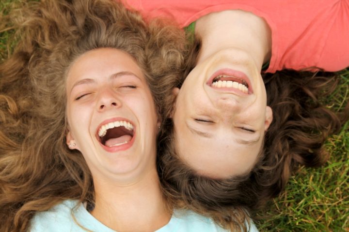 Две подруги смеются лежа на траве 
