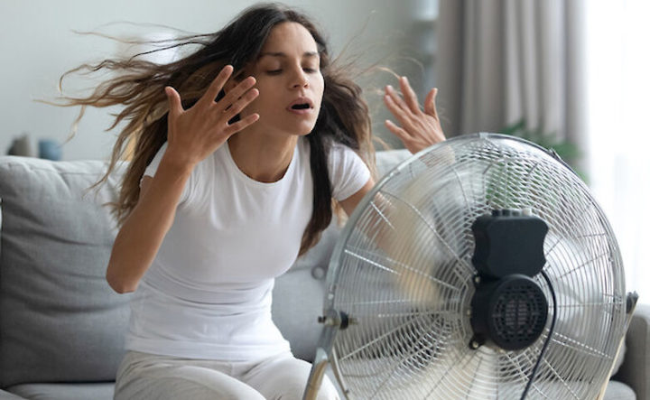 Девушка сидит перед вентилятором и машет на себя руками