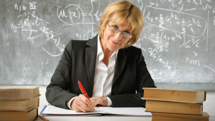 Учительница математики за столом на фоне доски