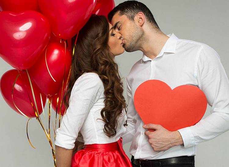 Влюбленная пара целуется и держит сердца из бумаги и воздушных шариков