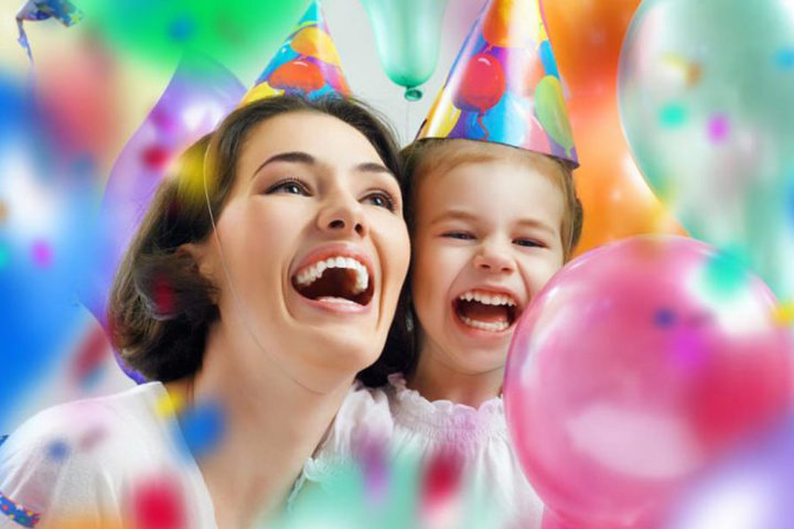 Смеющаяся женщина с ребенком в праздничных колпаках в воздушных шарах